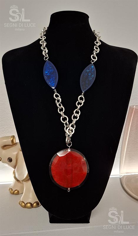 Collana statement artigianale con pietre blu a mandorla e disco centrale rosso, design scultoreo a forte contrasto cromatico.